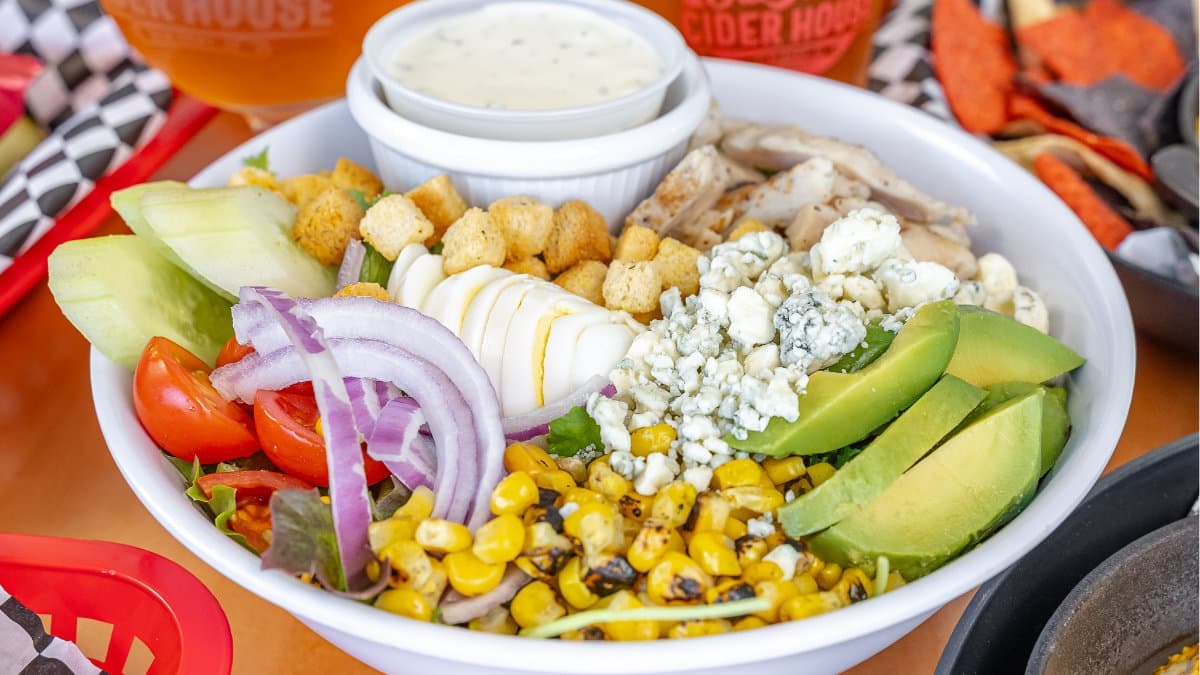 A chicken salad with avocado, corn, egg, and blue cheese
