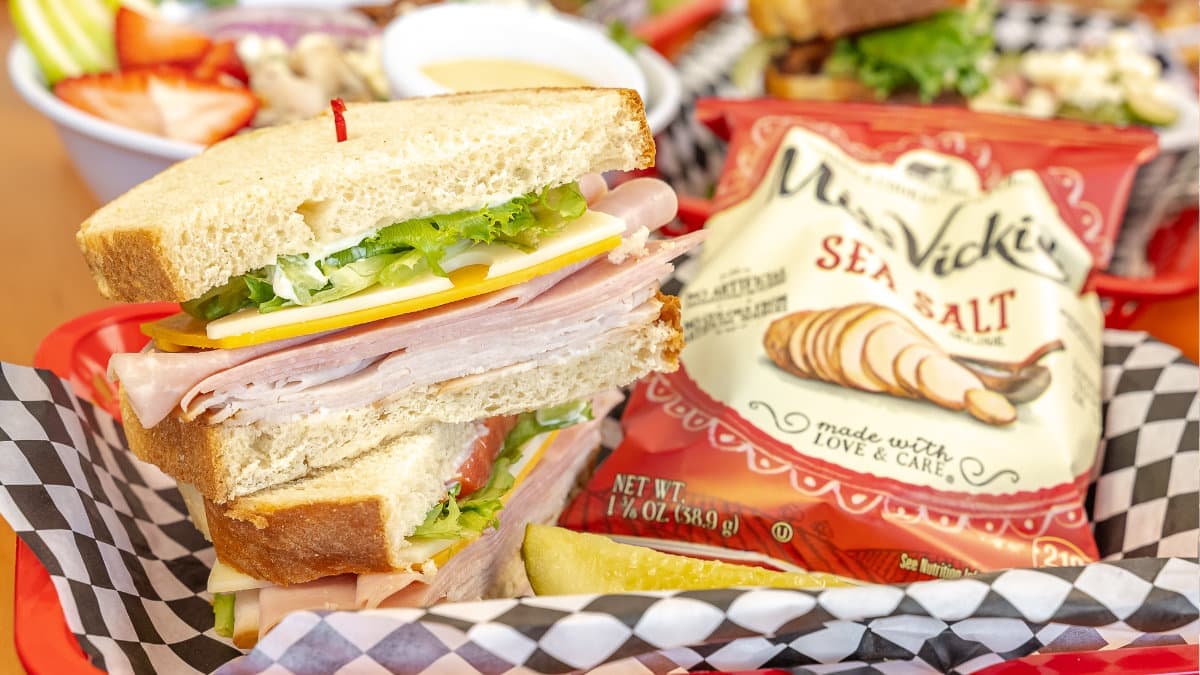 A stacked ham and cheese sandwich with chips and a pickle